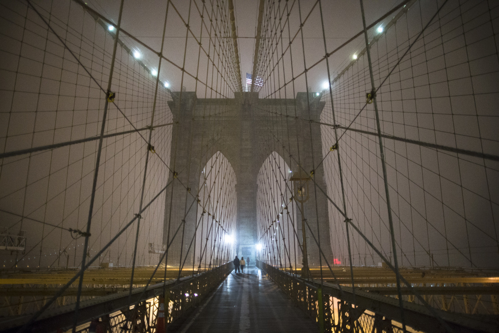 Pedestrians pass along a walkway under falling snow on the Brooklyn Bridge, Friday in New York.