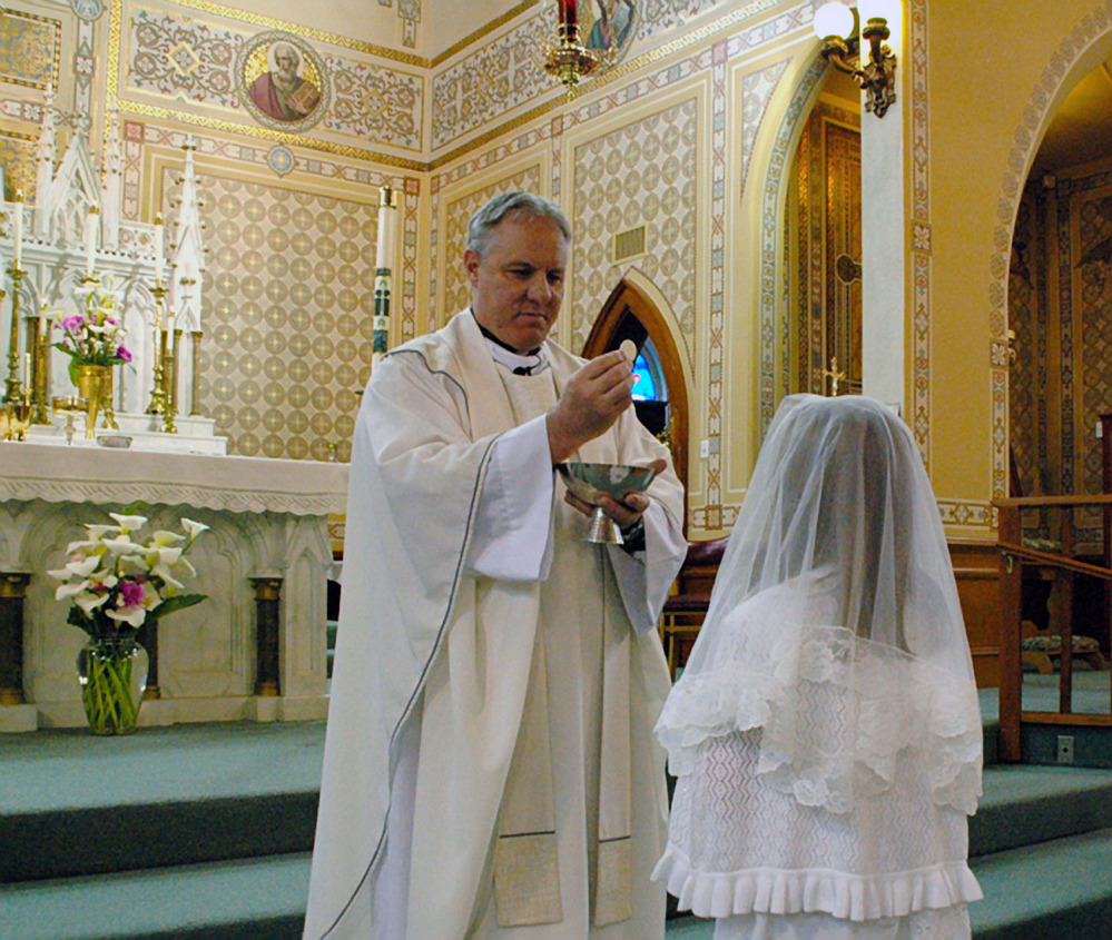 This May 2012 photo provided by Lynn Enemark shows the Rev. Eric Freed administering First Communion in St. Bernard Catholic Church in Eureka, Calif. Freed was found slain New Year’s Day in the rectory of the church. A suspect has been arrested who police say was in jail the day before behaving erratically but was released after being evaluated at a hospital.