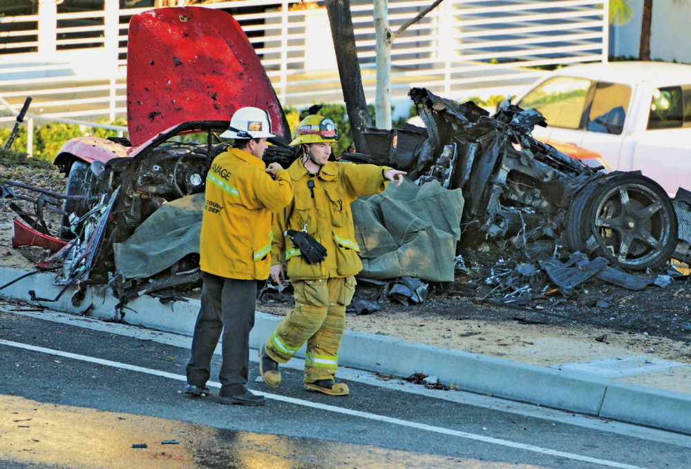 In this Nov. 30, 2013, photo, sheriff’s deputies work near the wreckage of a 2005 Porsche Carrera GT that crashed into a light pole in Valencia, Calif. The Los Angeles County coroner’s office says that Roger Rodas, Paul Walker’s friend and financial adviser, was driving the car at an unsafe speed.