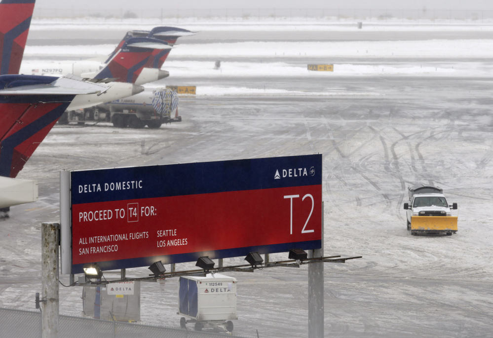 A snowplow makes its way on a slushy patch between two terminals after a Delta flight from Toronto to New York skidded off the runway into snow at Kennedy International Airport, temporarily halting all air travel into and out of the airport on Sunday.
