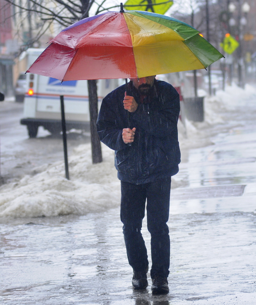 ELEMENTS: Wes Sproul walks over ice Monday on Water Street in Augusta while getting a cup of coffee. Several inches of rain fell on snow and crust, creating hazardous conditions outside.