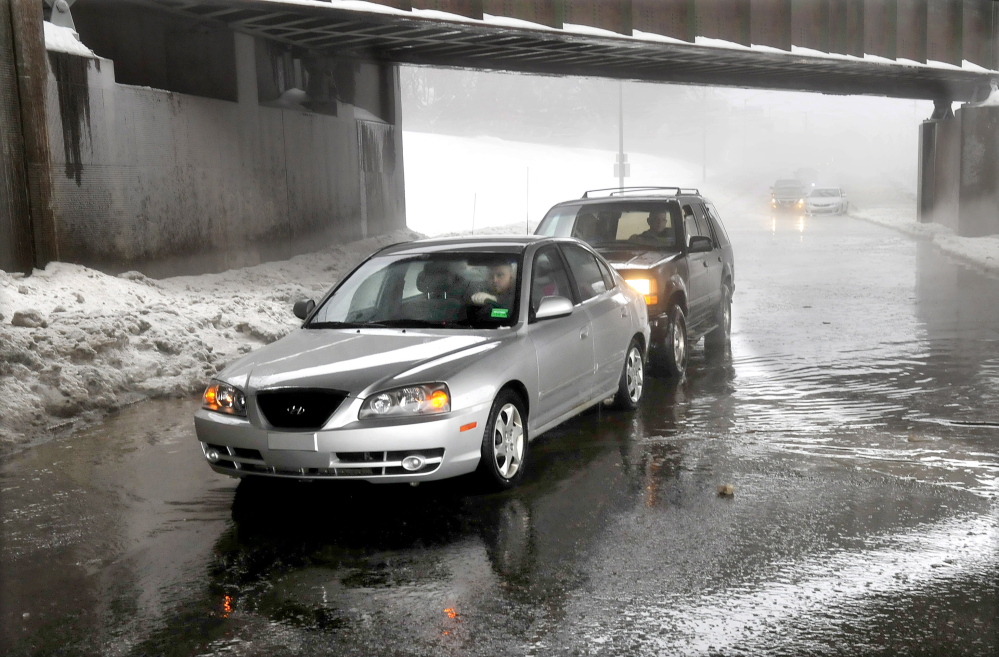 PUSHED OUT: Motorist Derek Archer, in the front car, is pushed out of a foot of water on College Avenue in Waterville during steady rain on Monday. Mark Farino came along and slowly pushed Archer’s vehicle out. Area streets and roads were flooded as drains were plugged and could not handle the volume of water.