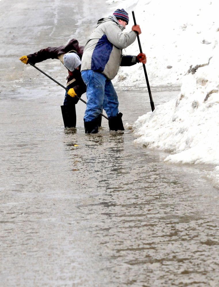 OVERWHELMED: Maxim Turmelle, left, and his uncle Arthur Turmelle search for a plugged storm drain in Waterville on Monday. “We called the city but they were overwhelmed with flooding calls so we did it,” Arthur Turmelle said.