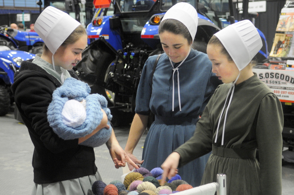 AGRICULTURE: Lilia, left, Cassia and Moriah Higgins inspect yarn Tuesday on display on the first day of the Maine Agricultural Trades Show at the Augusta Civic Center. Several thousand people were expected to attend the annual event for Maine farmers. The Higgins sisters raise sheep and pygmy goats at Fruitful Acres Farm in Newport. Lilia is holding family friend Naphtali Kulp, 1 month old.