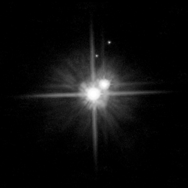 It’s cold out there: Pluto and its moons cold in the distant glitter of the sun. Pluto is the large orb at center of image. Charon is the next larger orb to its right.