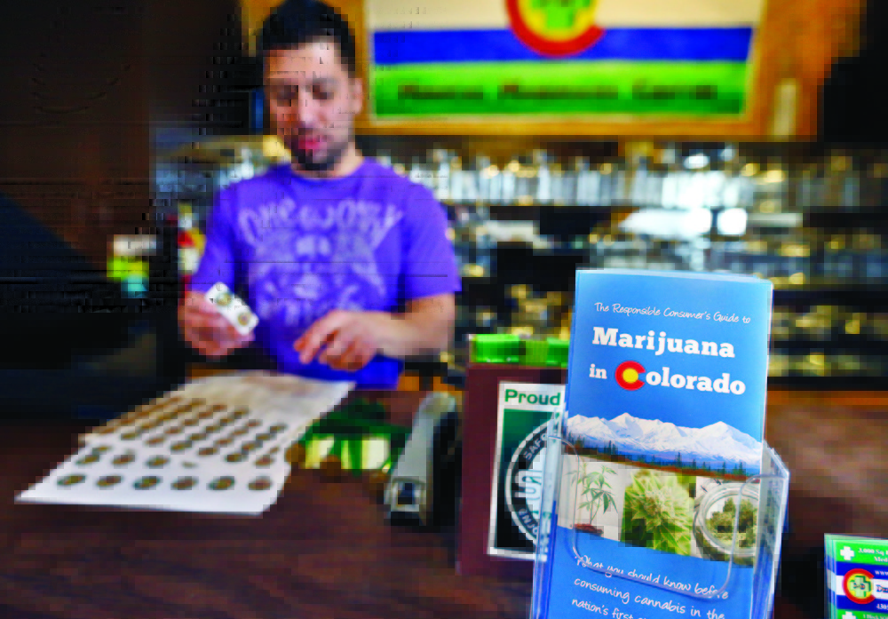General manager David Martinez labels containers of retail marijuana, behind a sales bar fitted with a brochure available to customers, at 3D Cannabis Center in Denver, Tuesday Dec. 31, 2013. Colorado is making final preparations for marijuana sales to begin Jan. 1, a day some are calling "Green Wednesday." The 3D Cannabis Center will be open as a recreational retail outlet on New Year's Day. (AP Photo/Brennan Linsley)