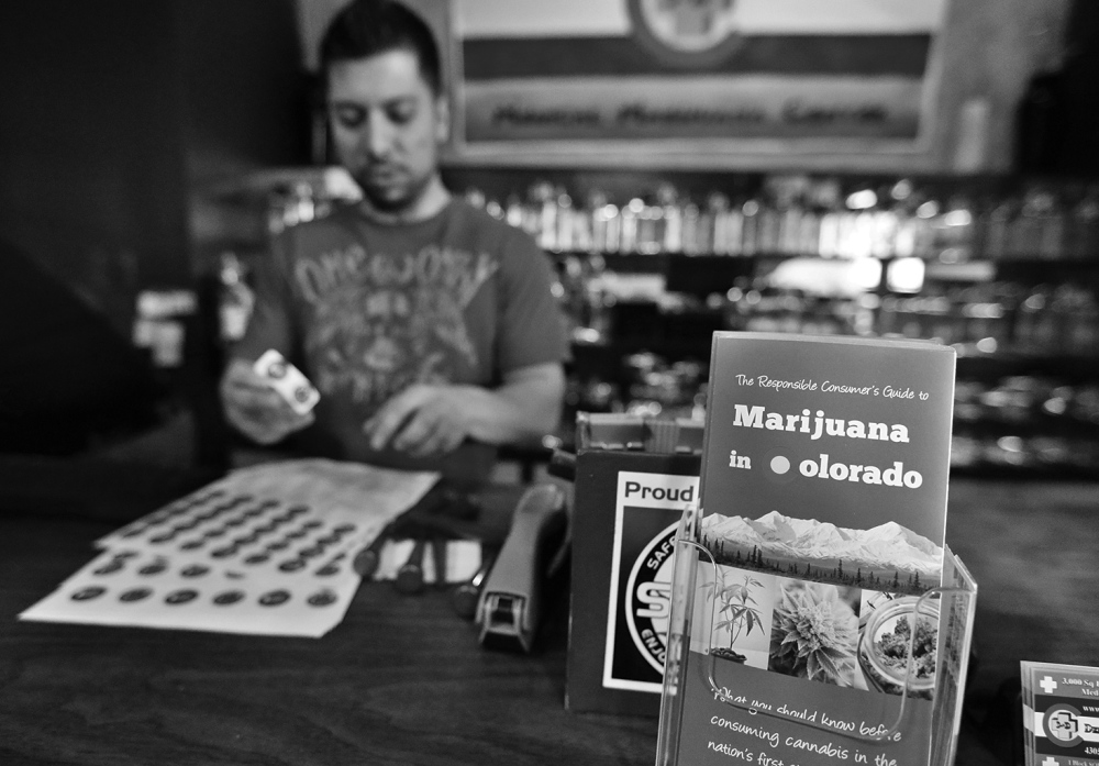 General manager David Martinez labels containers of retail marijuana, behind a sales bar fitted with a brochure available to customers, at 3D Cannabis Center in Denver, Tuesday Dec. 31, 2013. Colorado is making final preparations for marijuana sales to begin Jan. 1, a day some are calling "Green Wednesday." The 3D Cannabis Center will be open as a recreational retail outlet on New Year's Day. (AP Photo/Brennan Linsley)