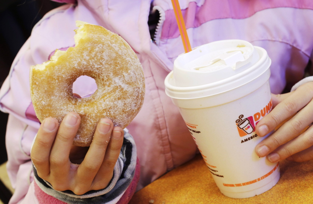 FILE - In this Feb. 14, 2013 file photo, a girl holds a beverage, served in a foam cup, and a donut at a Dunkin' Donuts in New York. Takeout-craving New York City is pondering whether to outlaw plastic foam to-go cups and trays, unless a yearlong inquiry shows they can be recycled effectively. (AP Photo/Mark Lennihan, File)