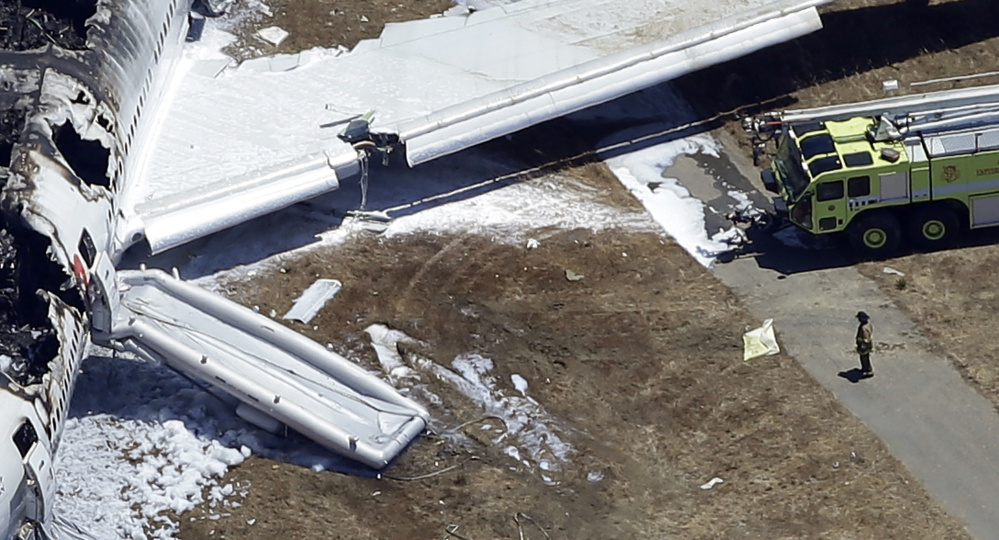 In this July 6, 2013, aerial photo, a firefighter stands by a tarpaulin sheet covering a body near the wreckage of the Asiana Flight 214 jet after it crashed at the San Francisco International Airport in San Francisco