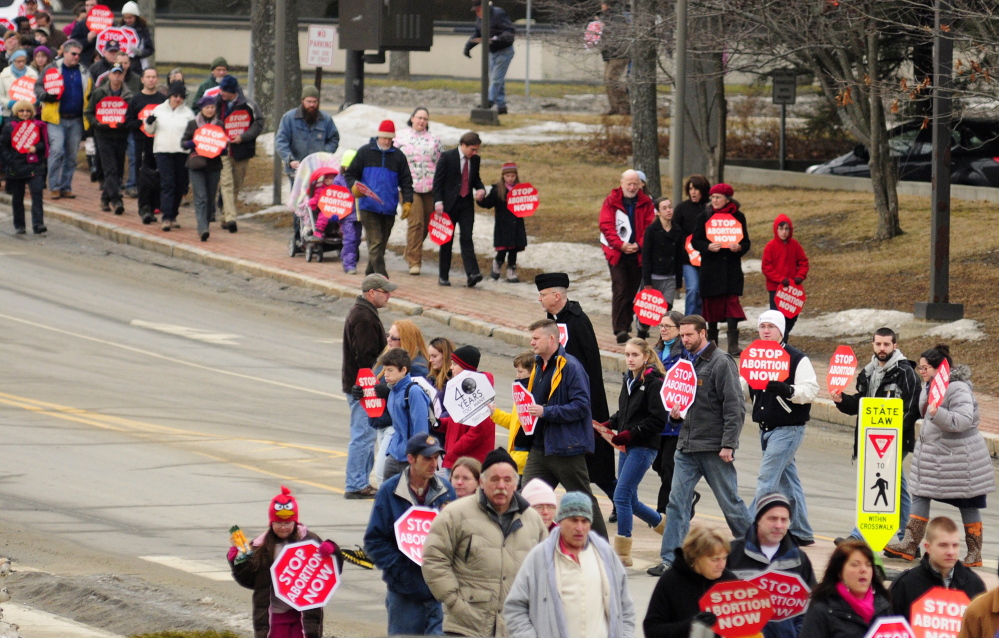 Signs of the times: Anti-abortion protesters cross Capitol Street on Saturday on their way to take part in the Hands Around the Capitol Memorial at the State House, in Augusta. The group held hands around the State House and rang a bell there 41 times during the event held to mark the 41st anniversary of the Supreme Court’s Roe v. Wade decision.