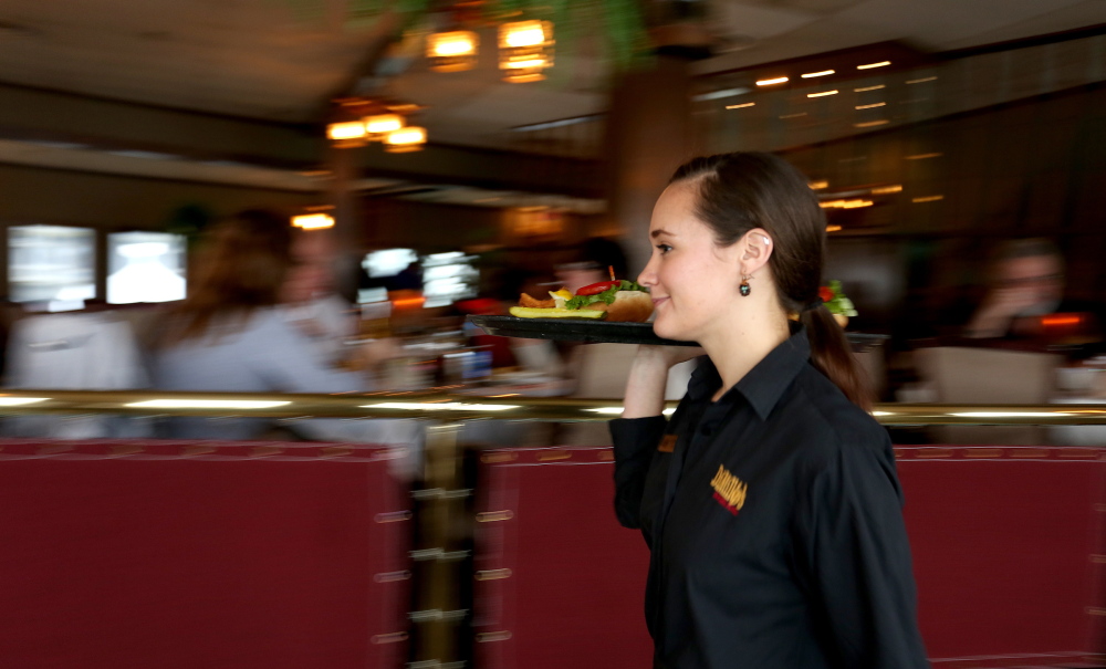 Cameron McManus, a server at DiMillo’s On the Water, carries lunch to diners. A tax code change has prompted some restaurants, like DiMillo’s, to end automatic gratuities for large dining parties. Some waitstaff worry that tips will be overlooked or reduced as a result.