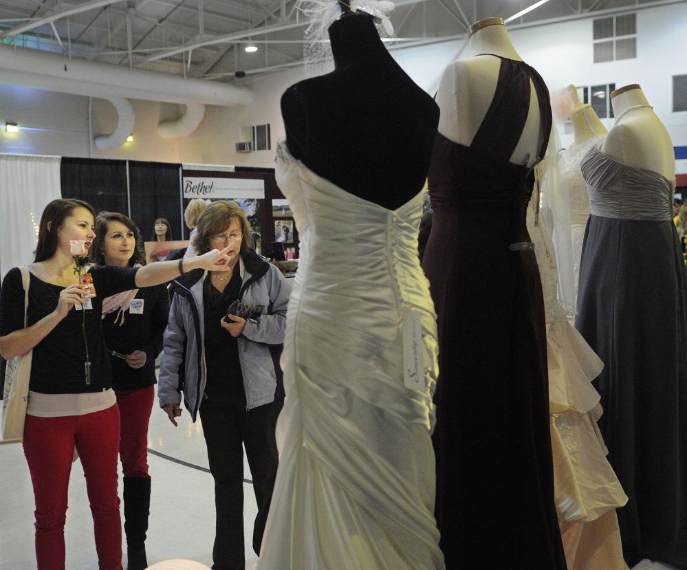 Say yes: Chantelle Osgood, left, her sister, Jenna Osgood, and mother, Lori Osgood, inspect wedding gowns on display at the Hussey’s General Store’s booth at the 22nd Annual Augusta Wedding Show at the Augusta Armory. The elder Osgood, of Madison, is marrying off both daughters within the year.