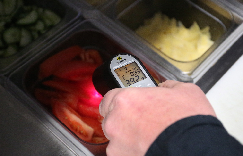 Portland Health Inspector Tom Williams uses a thermometer on Friday to check the temperature of standing vegetables at Buck’s Naked BBQ on Wharf Street. A bill would give all Maine communities freedom to inspect restaurants.