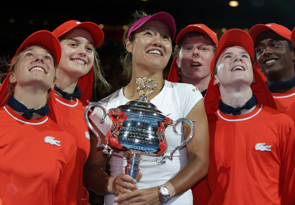 Li Na holds the championship trophy after defeating Dominika Cibulkova in their women’s singles final at the Australian Open tennis championship in Melbourne, Australia, on Saturday. She is accompanied by the tournament's ball boys and girls.