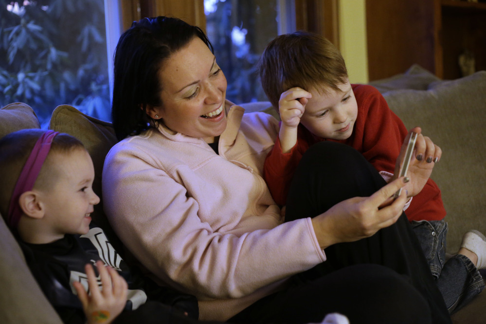 Julie Young, a Boston-based behavioral analyst, center, sits with her sons Nolan, 3, left, and Jameson, 4, while looking at a smart phone at their home, in Boston.
