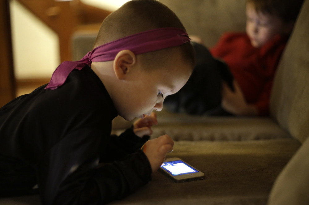 Nolan Young, 3, looks at a smart phone while his brother Jameson, 4, right, looks at a smart tablet at their home in Boston on Monday.