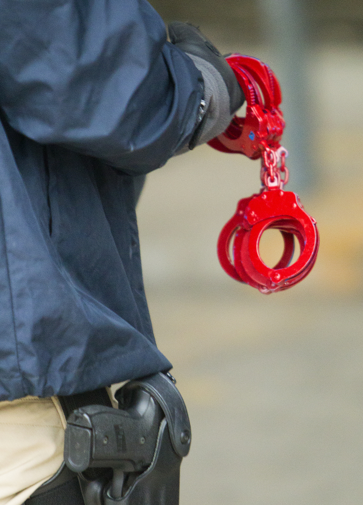 An official, holding handcuffs, prepares to arrest suspects after raiding a business, Thursday, Jan. 30, 2014, in southwest Houston.