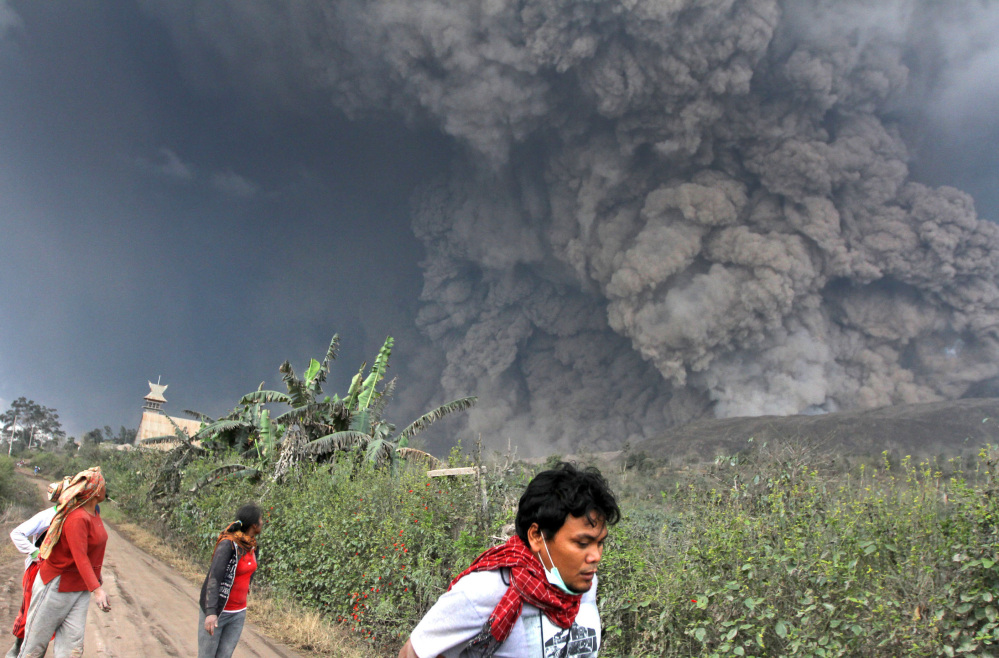 Villagers and a journalist flee as Mount Sinabung, which has been rumbling for four months, erupts in Indonesia, Saturday. Some 14,000 people had just returned to the area, because the volcano had seemed less active.