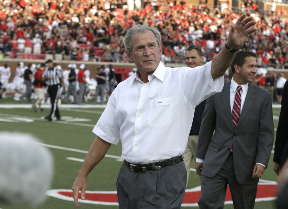 Former President George W. Bush waves as he walks off the field after the coin toss before the college football game between Texas Tech and Southern Methodist on Aug. 30, 2013, in Dallas.