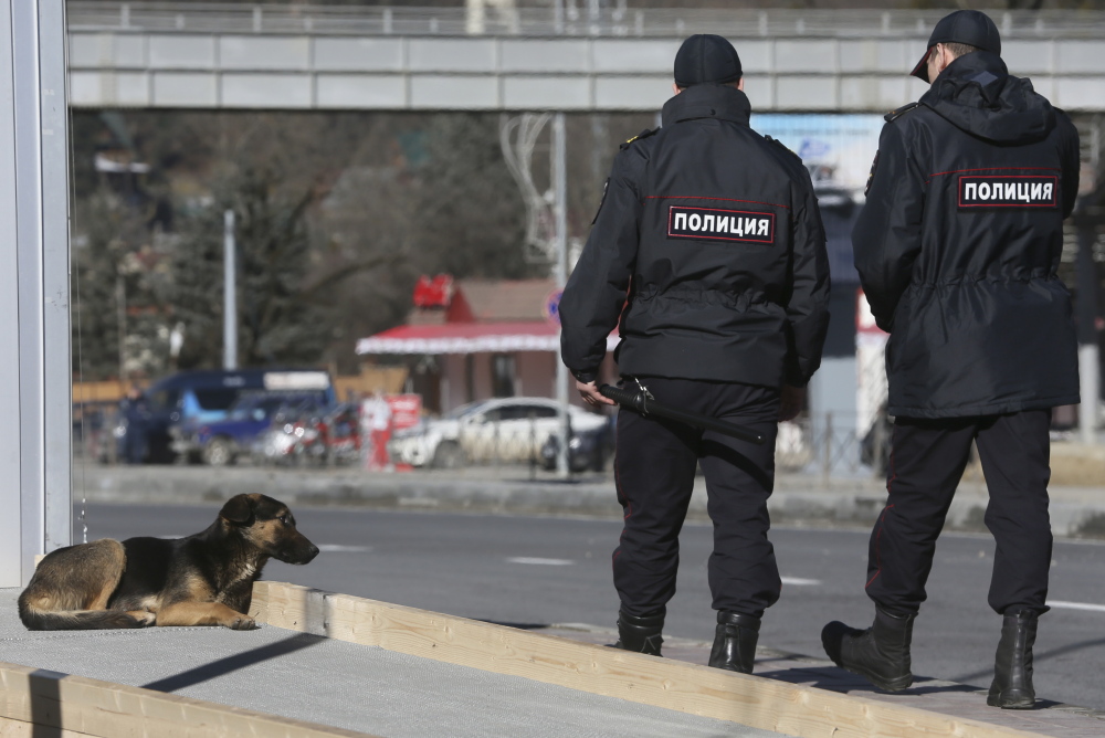 Policemen walk past a stray dog near the Media Center of the 2014 Winter Olympics on Monday in Krasnaya Polyana, Russia. Sochi authorities have hired a company to kill the packs of stray dogs to avoid Olympics embarrassment.