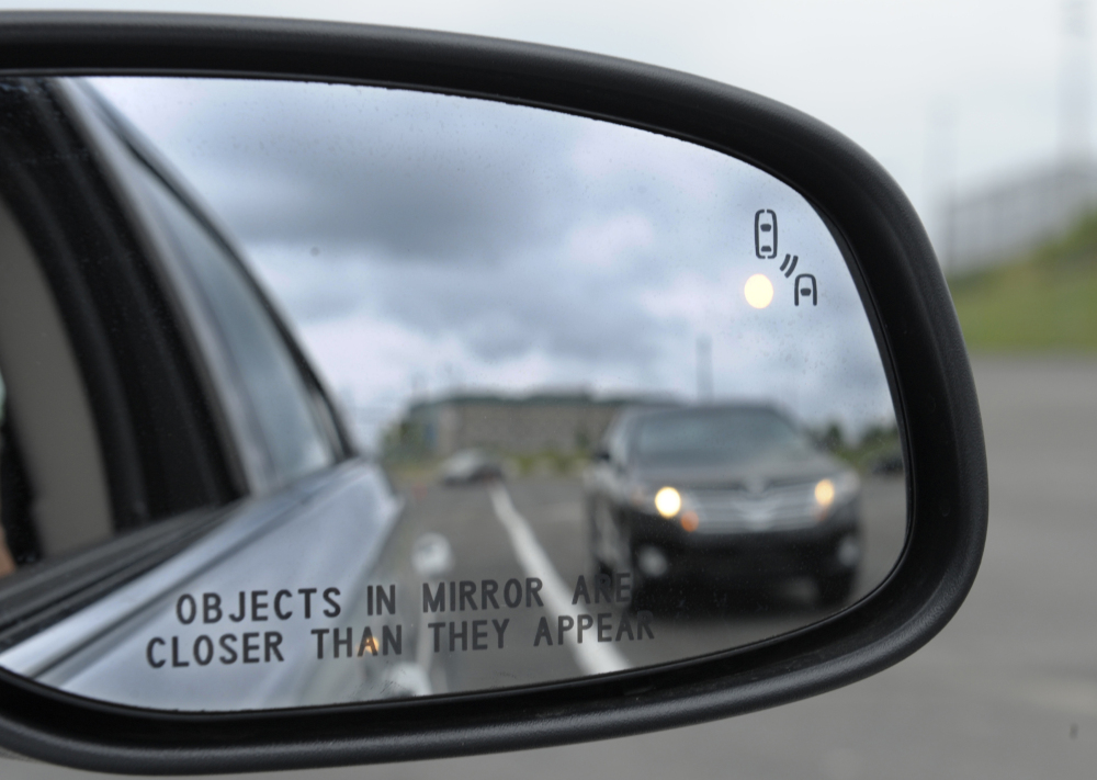 A side mirror on a Ford Taurus shows a collision warning signal at an automobile testing area in Oxon Hill, Md. Federal officials announced Monday that they will push to require automakers to equip new cars and light trucks with technology that enables vehicles to communicate with each other.