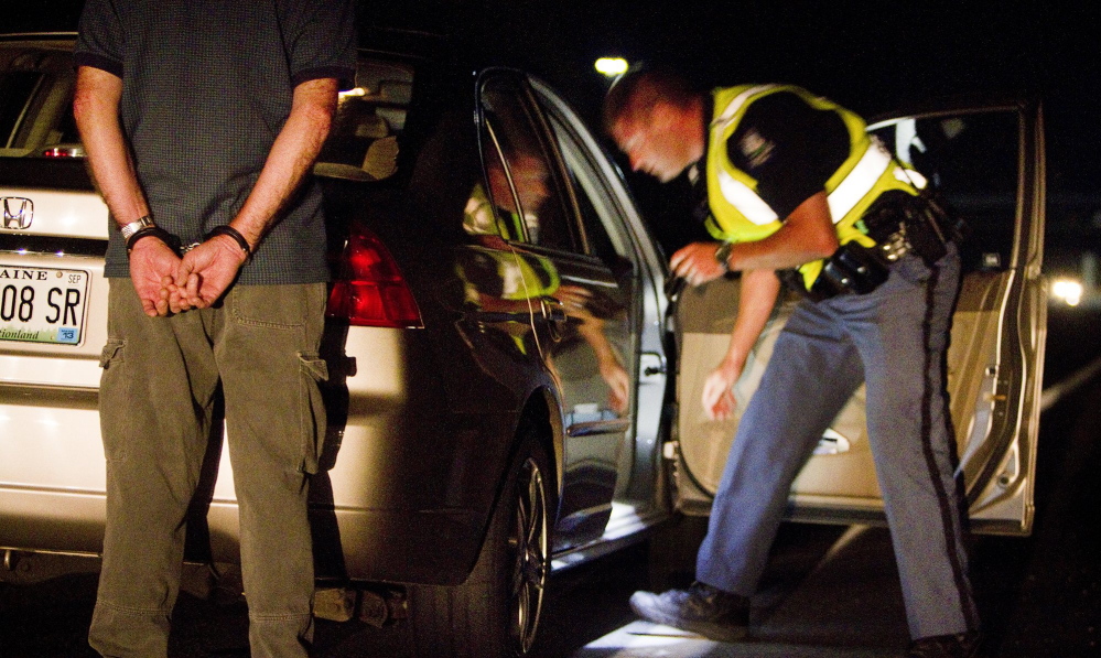 Cumberland police Officer Ryan Martin checks the contents of a vehicle as the driver, suspected of drunken driving, waits behind the car in handcuffs, during a Cumberland County sobriety check in Brunswick in August. A bill under consideration in Augusta would extend the time frame for charging a driver as a repeat offender.