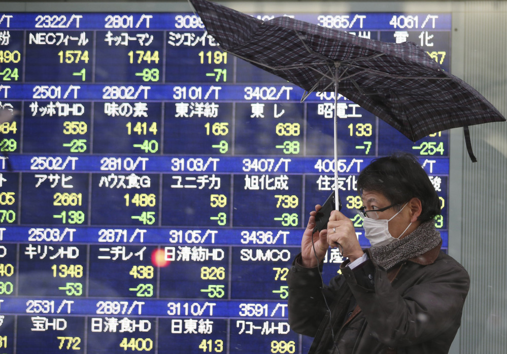 A man reacts to a gust of wind as it starts to snow in front of an electronic stock board at a securities firm in Tokyo Tuesday. Japan’s Nikkei 225 stock average dived more than 4 percent Tuesday as weakness in U.S. and Chinese manufacturing sent Asian markets sharply lower. The Nikkei tumbled 4.2 percent to 14,008.47 and is down 14 percent over the past month.