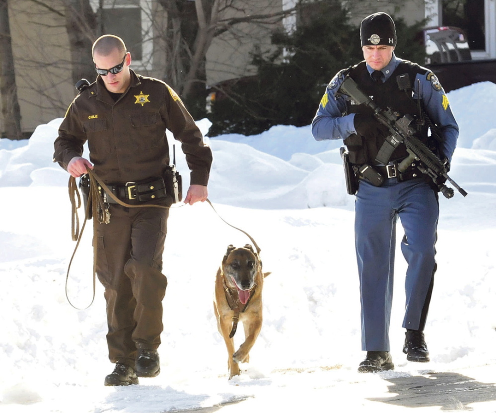 SEARCH: Somerset Sheriff’s Deputy David Cole, left, and tracking dog Ruger, along with Trooper Peter Michaud, search the parking lot of Skowhegan Savings bank in Bingham after a man with a hammer robbed the bank on Tuesday.