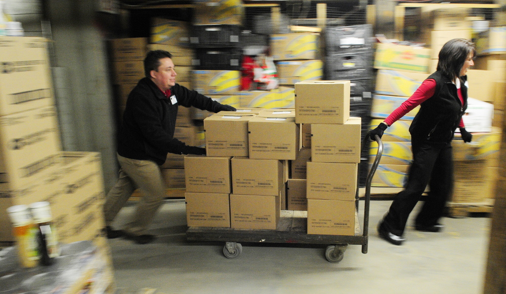 Staff photo by Joe Phelan HELPING HANDS: Hannaford employees Lee Lemar, left, and Marie Tardiff, roll a cart loaded with donated food on Friday February 7, 2014 at the Augusta Food Bank’s warehouse.