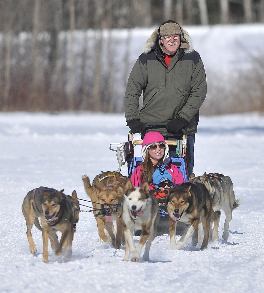 Dog Sleding: David Farr, a musher with Heywood Kennel Sled Dog Adventures in Augusta, drives a team of dogs with Elaine George and her son Alexander, 2, on board during the annual Winter Carnival at Quarry Road Recreational Area in Waterville on Saturday.