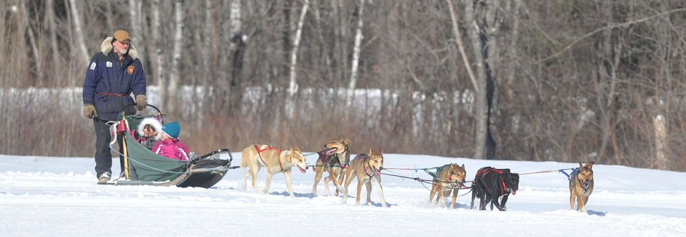 Mush: Kevin Quist, a musher with Heywood Kennels Dog Sled Adventures in Augusta, drives a team of dogs with Jackie Bean, 11, back, and Zoie Ouellette, 5, front, on board during Winter Carnival at Quarry Road Recreational Area in Waterville on Saturday.