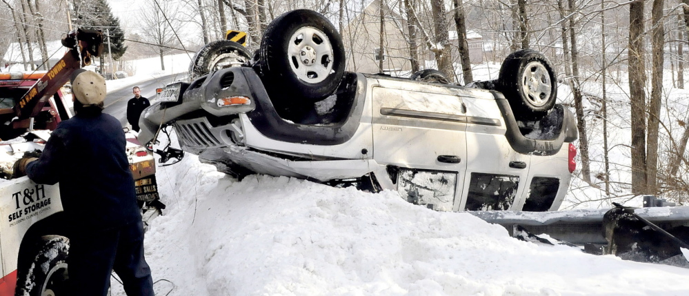 BENTON ROLLOVER: Reid Liberty, background, of Benton, watches as one of two tow truck operators pulls his car out of a ravine after the Jeep slid on ice, went over a guardrail and rolled over into the woods on Route 100 in Benton on Monday. Liberty was not injured.