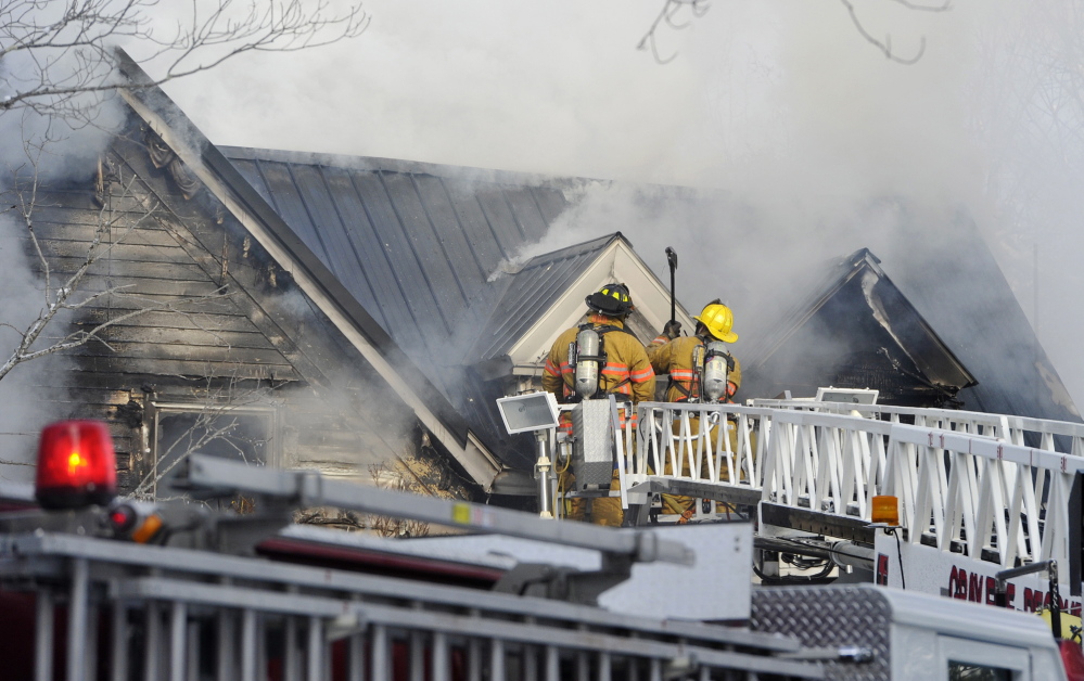 Firefighters use axes from their perches on a ladder truck to access flames while fighting a fire at 16 Weymouth Road in Gray on Monday morning.