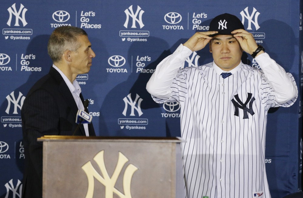 PUTTING ON THE PINSTRIPES: New York Yankees pitcher Masahiro Tanaka puts on his hat and jersey as manager Joe Girardi watches him during a news conference Tuesday at Yankee Stadium in New York.