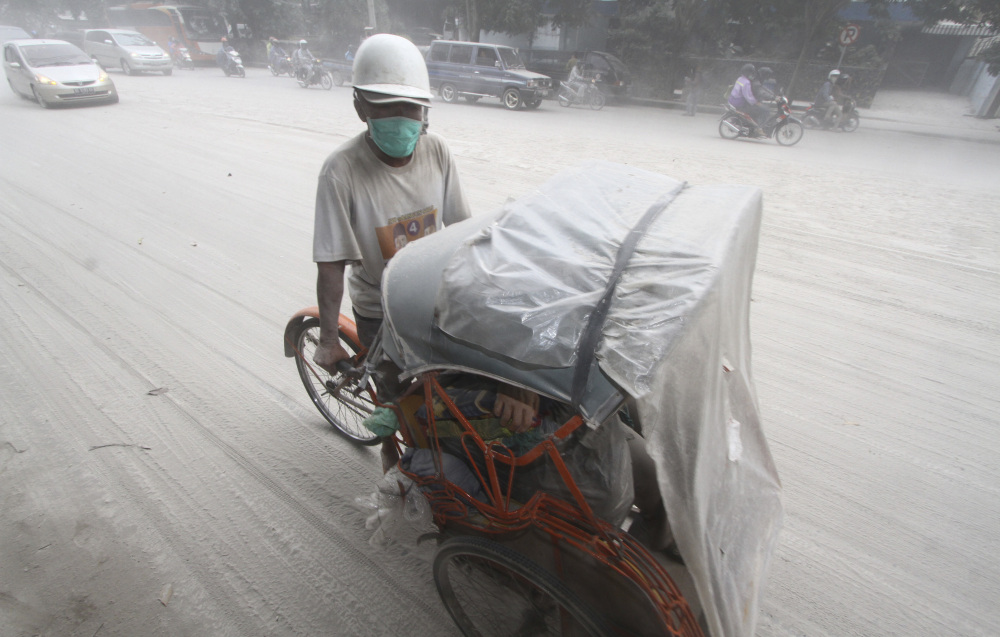 A pedicab makes its way on a street covered with volcanic ash in Solo, Indonesia on Friday