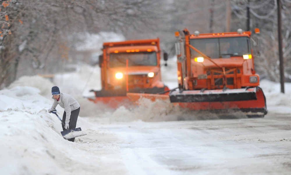 NEVERENDING JOB: Melinda Hansen tries to shovel her driveway on North Street in Waterville earlier this winter as two Waterville plow trucks bear down on her efforts..