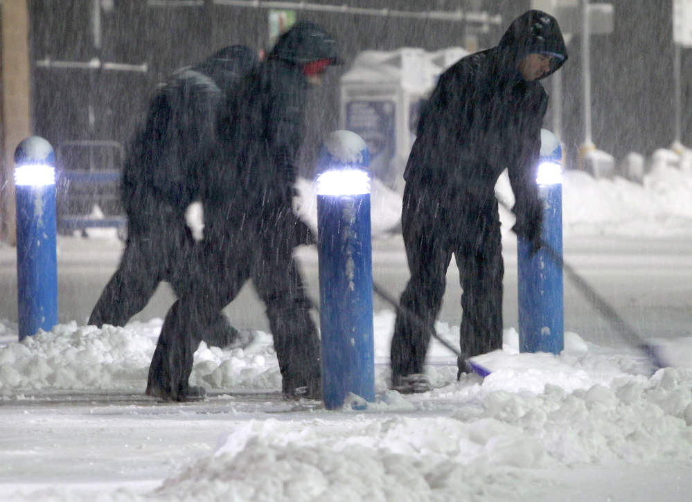 Workers clears snow from the sidewalk outside a business Saturday in the Boston suburb of Hudson, Mass.
