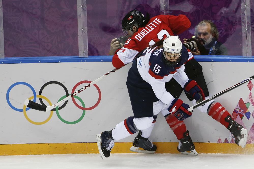 Anne Schleper of the United States (15) pins Caroline Ouellette of Canada (13) against the boards during the first period of the women’s gold medal ice hockey game at the 2014 Winter Olympics Thursday in Sochi, Russia.