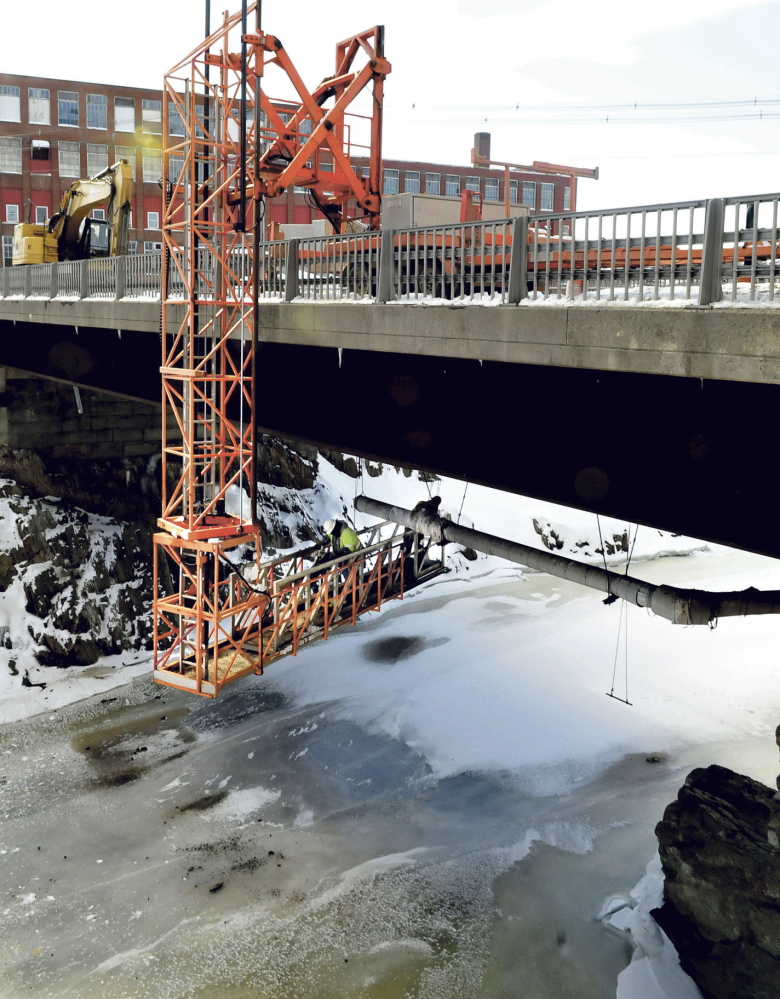 OVER AND UNDER: Workers are suspended under one of the Margaret Chase Smith Bridges in Skowhegan while removing a sewer line recently. Other workers nearby are replacing a pumping station. All the work should be completed by April.