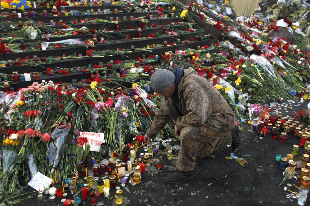 A man lights a candle at a memorial for the people killed in clashes with police at Independence Square in Kiev, Ukraine, Monday. Ukraine’s acting government issued a warrant Monday for the arrest of President Viktor Yanukovych, accusing him of mass crimes against protesters who stood up for months against his rule.