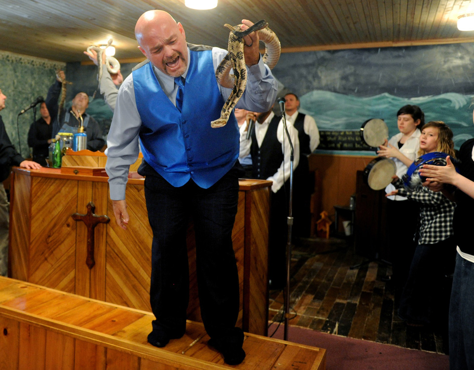 FILE - In this May 6, 2012 file photo, Jamie Coots, pastor of the Full Gospel Tabernacle in Jesus Name Church of Middlesboro, Ky, stands on a bench before the church, singing and holding a rattlesnake during service at Tabernacle Church of God in LaFollette, Tenn. on May 6, 2012.