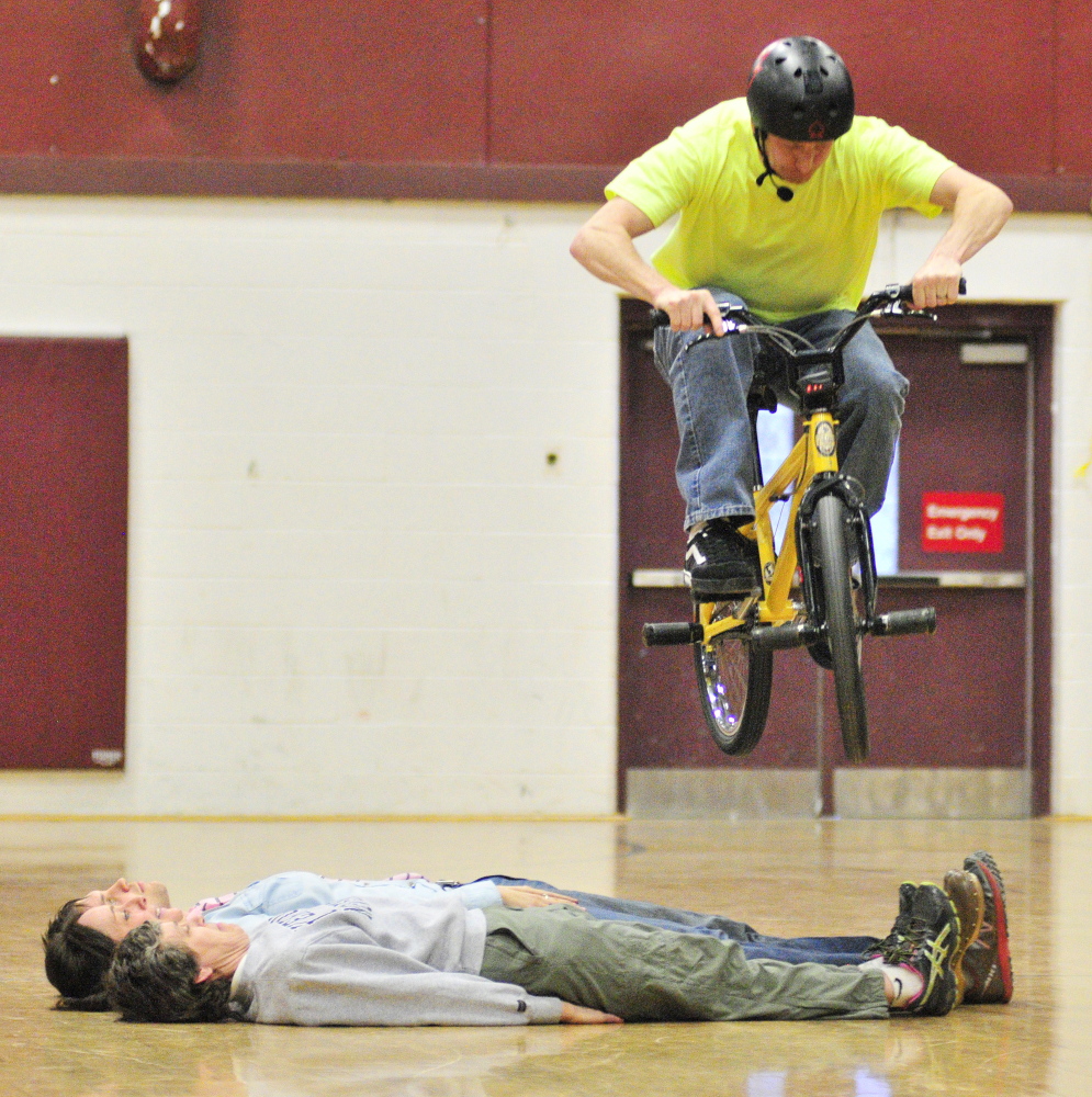 LIFE TRICKS: Chris Poulos, World Champion Bicycle Stunt Rider, Motivational Speaker and Author, jumps over three faculty members as the finale to his afternoon of bike tricks and a talk to Cottrell School students in the Foster Memorial Gym at Monmouth Academy on Friday.