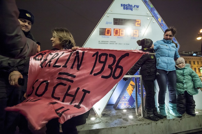 A gay rights activist holds a banner in front of a large clock showing the number of days left until the start of the Olympic games as police officers approach, left, in St. Petersburg, Russia, Wednesday, Feb. 5, 2014. Russian gay rights activists protested the upcoming Olympic Games in Sochi. Two activists unfurled banners reading “Berlin 1936 = Sochi 2014,” referring to the Olympic Games that were held in the capital of Nazi Germany. One-man pickets are legal in Russia and the two activists holding signs were spaced far enough apart that neither was arrested.