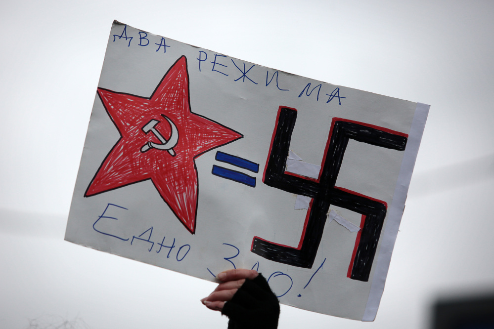 A Bulgarian protester holds a poster depicting Soviet-era Russian and Nazi symbols reading in Bulgarian “Two regimes, but one evil” during a protest in front of the Russian embassy in Sofia, Monday. Demonstrators condemned Russian military actions in Ukraine.