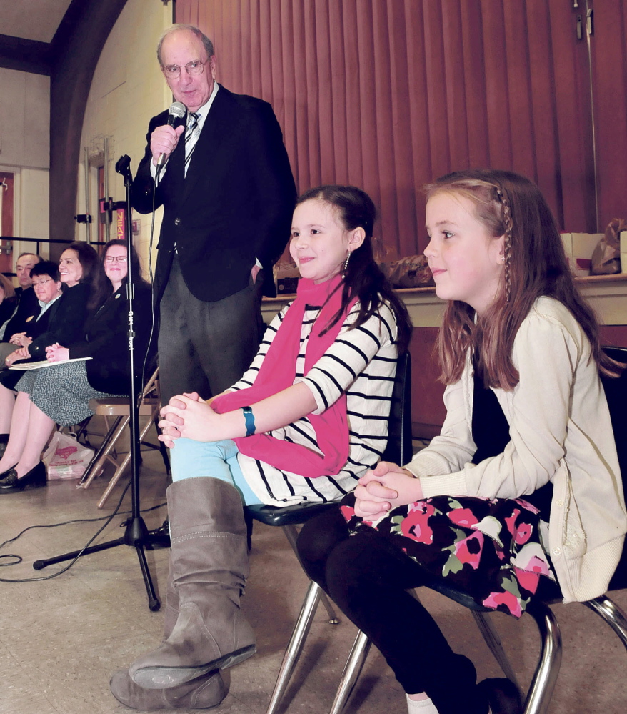 YOUNG STARS: Former U.S. Sen. George Mitchell pays tribute to students Gabbie St. Peter, left, and Alice Willette during an assembly Wednesday at George J. Mitchell School in Waterville. The second-graders were honored for their efforts to raise money and awareness for the school food pantry when they asked for donations rather than birthday presents.