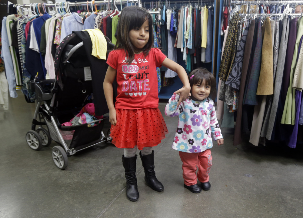 Two young girls hold hands as their mother sifts through used clothing at Sacred Heart Community Service recently in San Jose, Calif.