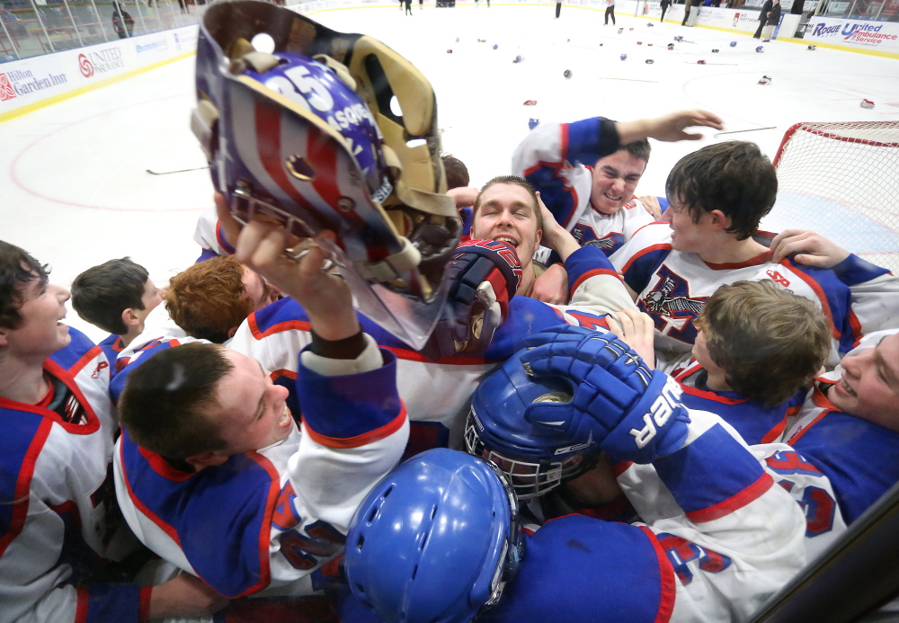 Messalonskee teammates mob their goalie Benjamin Weeks, center, as teammate Tyler Simpson, left, raises up his helmet after they defeated Gorham 6-1 in the Class B state championship on Saturday at the Colisee in Lewiston.