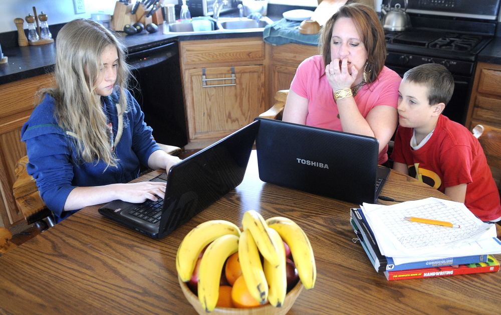 WAITING FOR VIRTUAL SCHOOL: Kyara Dawbin, 13, works on a lesson Thursday at the kitchen table with her mother, Karinna, and brother, Peter, 9, at their West Gardiner home. The Dawbins may enroll their children in Maine Connections Academy if the virtual school opens this fall.