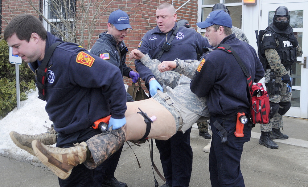 RETRIEVING THE WOUNDED: Augusta firefighters on Wednesday carry a Maine Army National Guard soldier from Camp Keyes in Augusta while Augusta Police Officer Niko Hample, right, protects them during an active-shooter drill at the Guard’s headquarters. Augusta emergency service workers collaborated with state and federal agencies to simulate a shoot-out and bombing at the post.