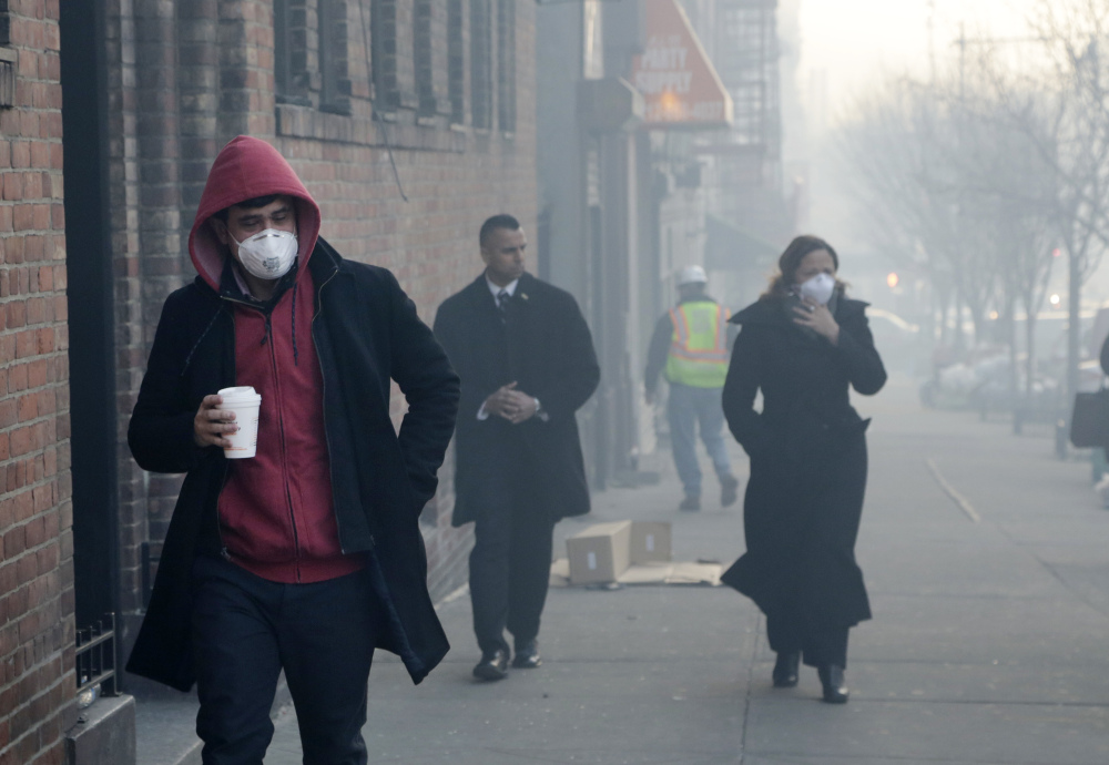 People wear dust masks as they walk near the explosion site in New York City Thursday. Rescuers working amid gusty winds, cold temperatures and billowing smoke pulled four additional bodies Thursday from the rubble of two East Harlem apartment buildings.